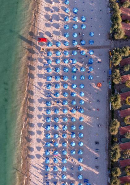 Spiaggia con ombrelloni blu e case vicine, vista dall'alto.