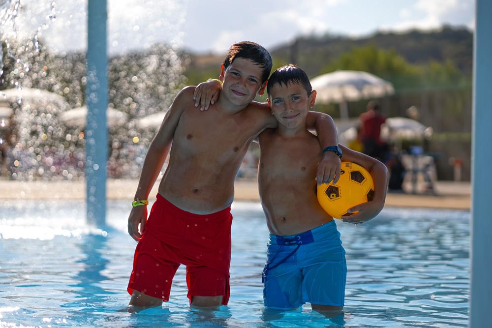 Deux garçons dans une piscine avec un ballon jaune.