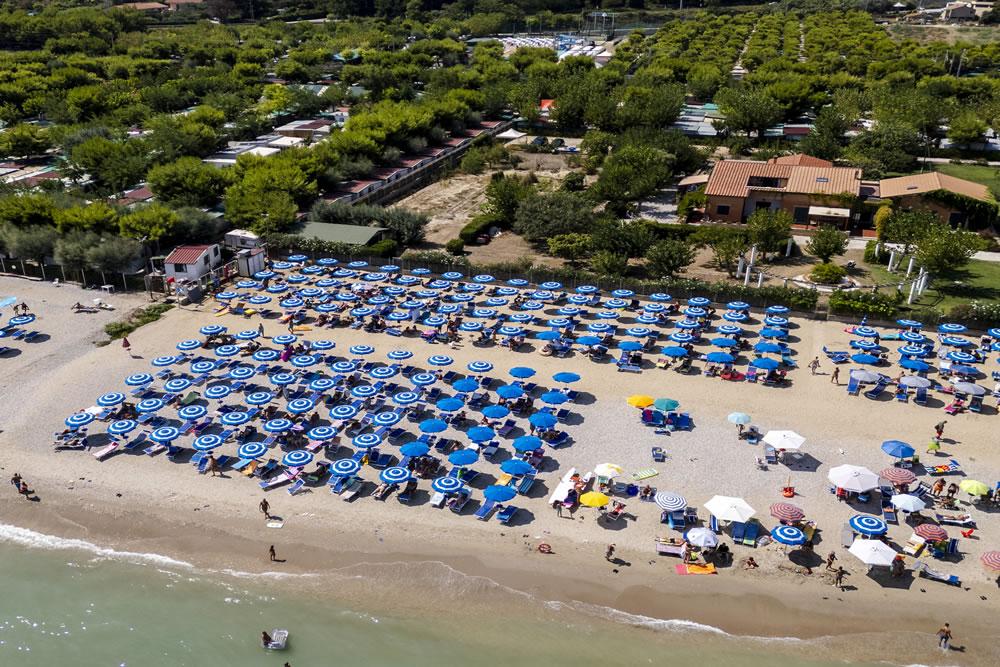 Plage bondée avec des parasols bleus et blancs, vue aérienne.