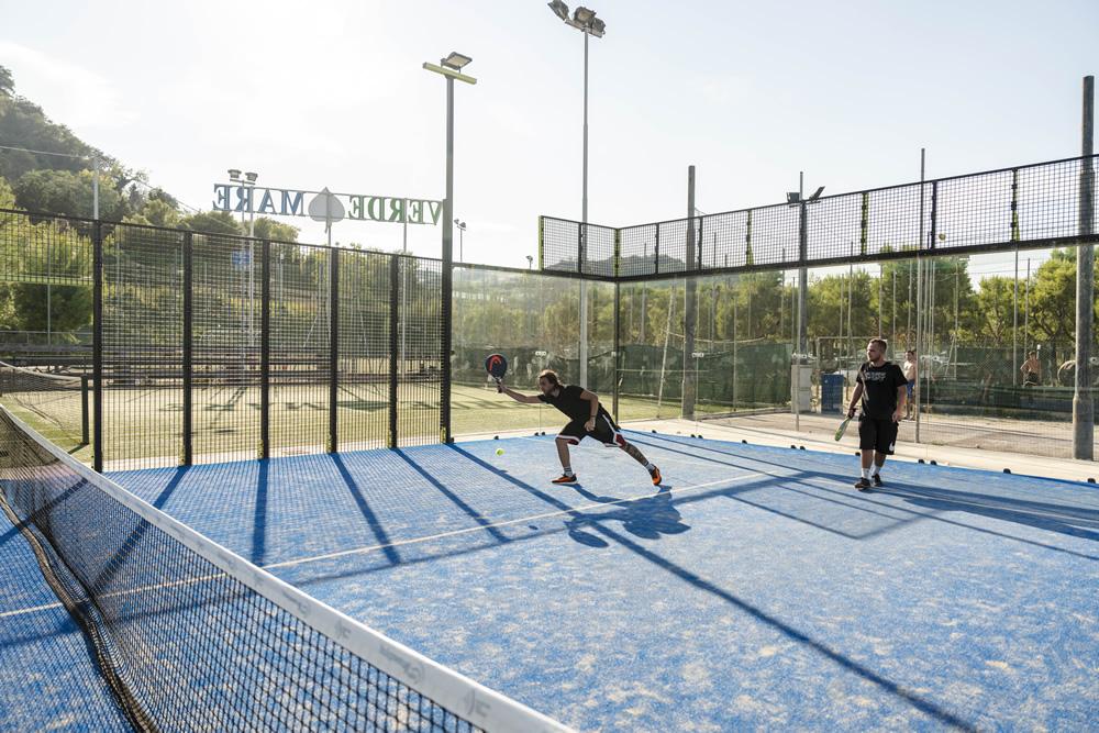 Deux personnes jouent au padel sur un court bleu extérieur.