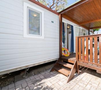 Maison mobile avec véranda en bois, entourée de verdure.