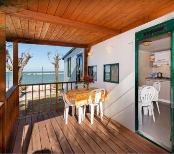 Véranda en bois avec vue sur la mer, table et chaises blanches.