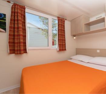 Chambre avec couverture orange et armoire murale.