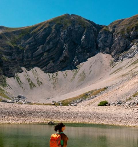 Wanderer betrachtet einen alpinen See unter einem felsigen Berg.