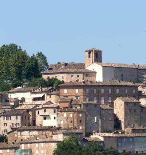 Italienisches Dorf mit Steinhäusern und Kirche auf einem grünen Hügel.