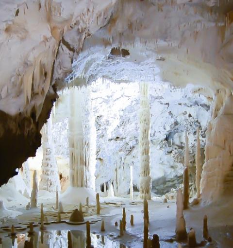 Höhle mit Stalaktiten und Stalagmiten im Wasser gespiegelt.