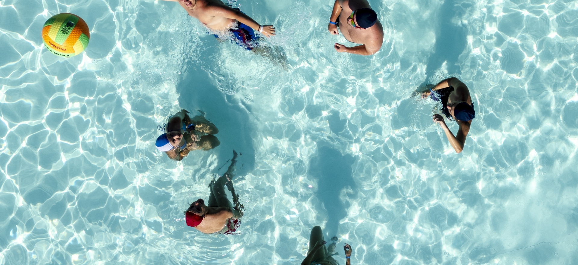 Des gens jouent au ballon dans une piscine vue d'en haut.