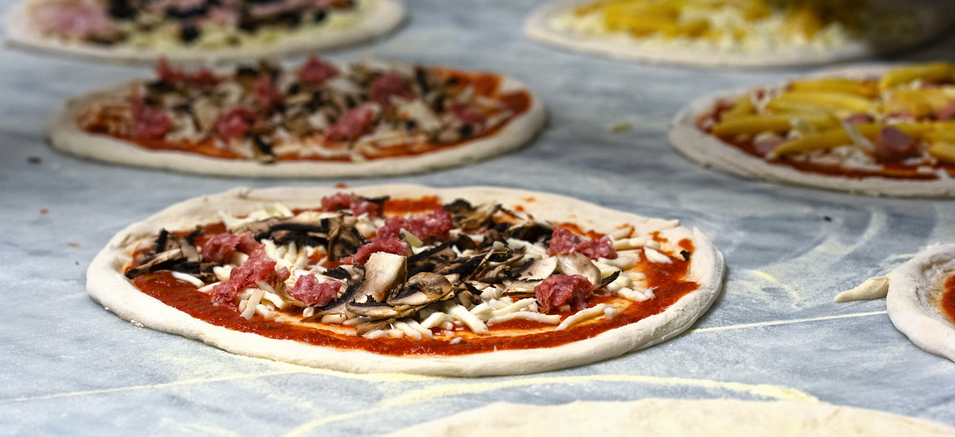 Rohe Pizzen mit verschiedenen Belägen auf einer Arbeitsfläche.